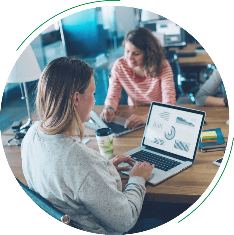 Two women sitting at a table with laptops.